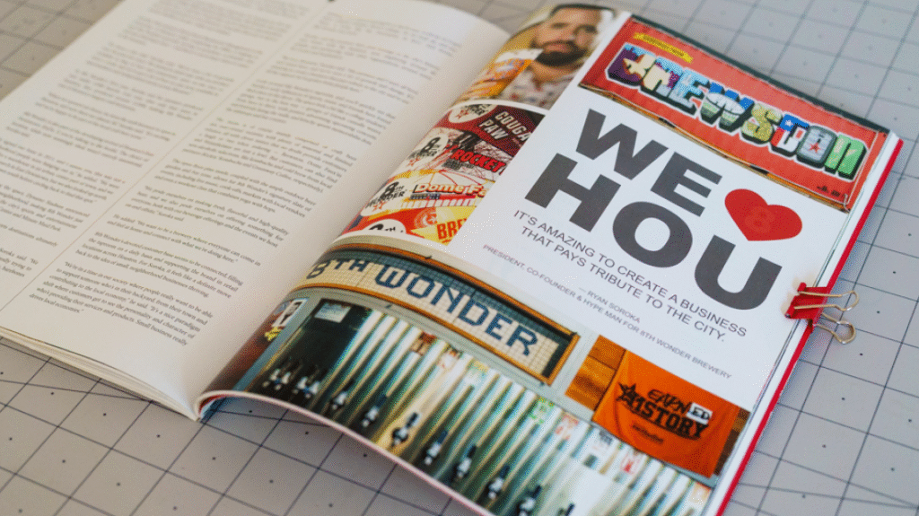 An open page of Inside Bauer Magazine. Left side: Two columns of text, illegible because of how the picture is taken. Right side: Photo collage and text section. Photo collage: : A mural that says "Brewston," a man holding a pint glass of beer, a bunch of felt triangle-shaped flags with various logos and sayings on them, a wall of beer taps with a sign above that reads "8th Wonder" and a flag next to the sign that reads "Earned History." Text section: We heart icon "HOU," "It's amazing to create a business that pays tribute to the city"